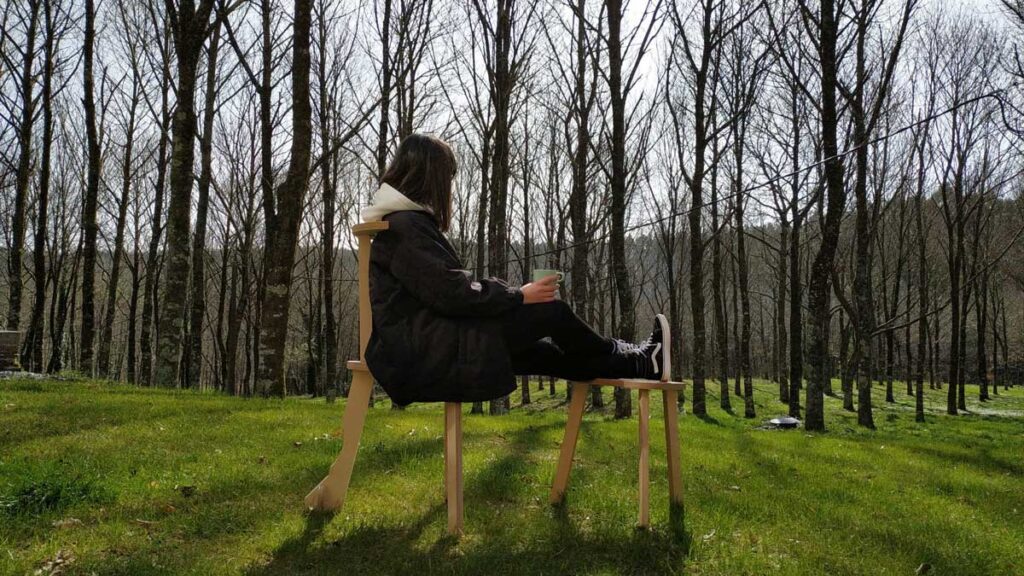 Fotografía de una chica en el bosque tomando una taza de té sentada en las sillas de madera. Proyectos de arquitectura del estudio de EEG Arquitectos en Pontevedra.